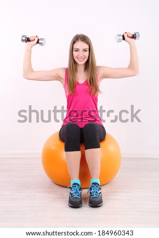 Young beautiful fitness girl exercising with orange ball and dumbbells in gym