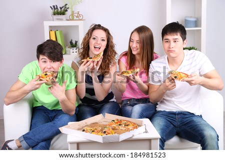 Group of young friends eating pizza in living-room on sofa