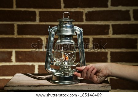 Hand lights a kerosene lamp on brick wall background