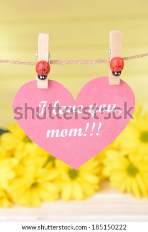 Happy Mothers Day message written on paper heart with flowers on yellow background