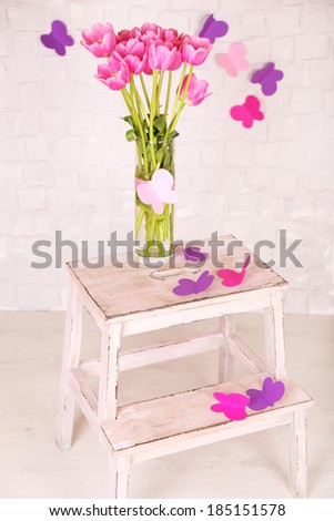 Composition with bouquet of tulips in vase, on chair, on wall background