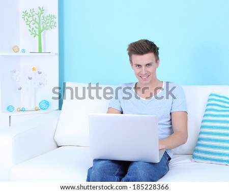 Guy sitting on sofa with laptop on blue background
