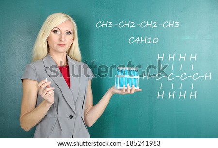 Chemistry teacher explaining formula written on blackboard to her pupils