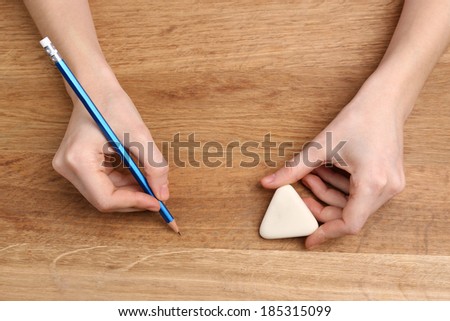 Human hands with pencil and erase rubber on wooden table background