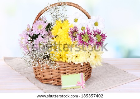 Beautiful chrysanthemum flowers in wicker basket on table on light background