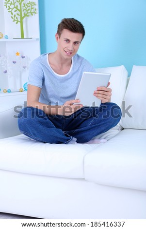 Guy sitting on sofa with electronic tablet on blue background