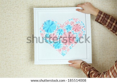 Woman hanging up picture with heart from paper flowers