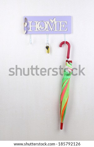 Umbrella and key hanging from hook, on light wall background