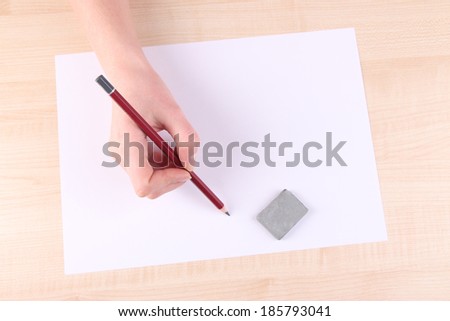 Hand holding pencil and erase with paper on wooden background
