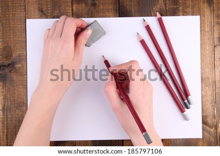 Hands holding pencil and erase with paper on wooden background