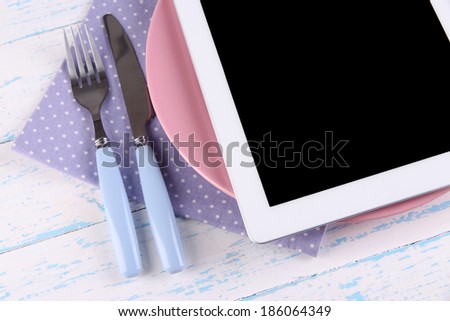 Tablet on plate with fork and knife on wooden background