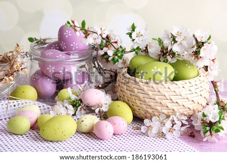 Composition with Easter eggs in glass jar and wicker basket, and blooming branches on light background