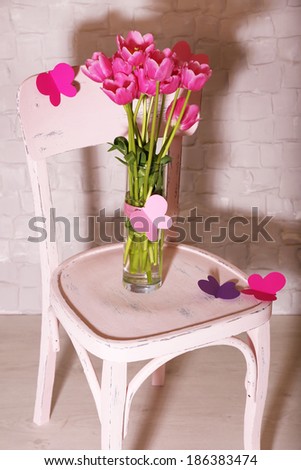 Composition with bouquet of tulips in vase, on chair, on wall background