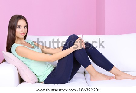 Beautiful young woman relaxing on sofa on pink background