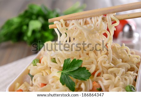 Tasty instant noodles with vegetables in bowl on table close-up