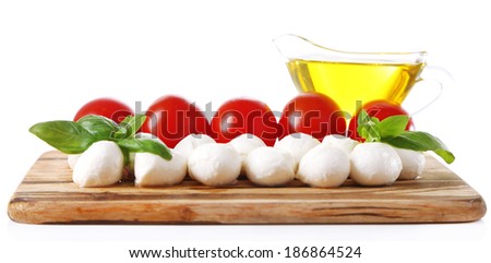 Composition with tasty mozzarella cheese balls, basil and red tomatoes, olive oil on cutting board, isolated on white