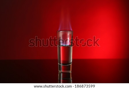 Glass with burning alcohol on red background