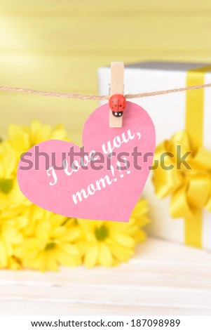 Happy Mothers Day message written on paper heart with flowers on yellow background