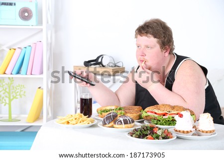 Fat man has a big lunch and watching TV, on home interior background