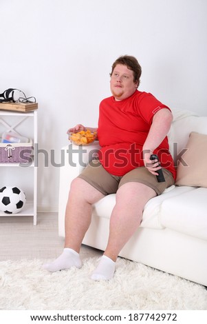 Lazy overweight male sitting on couch with chips and watching television