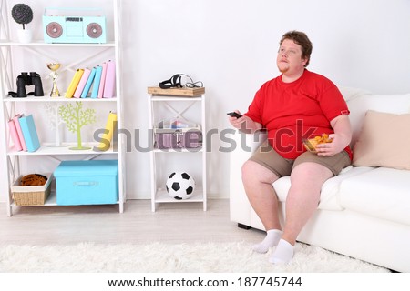 Lazy overweight male sitting on couch with chips and watching television
