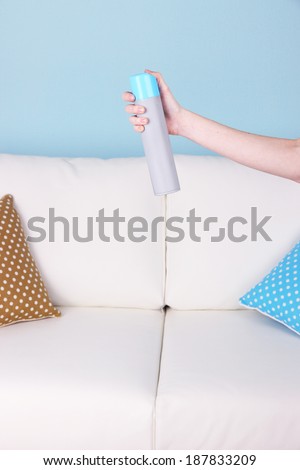 Sprayed air freshener in hand on sofa background
