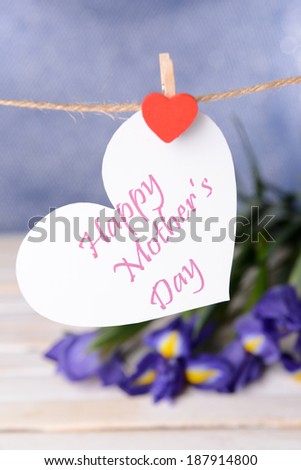 Happy Mothers Day message written on paper heart with flowers on purple background