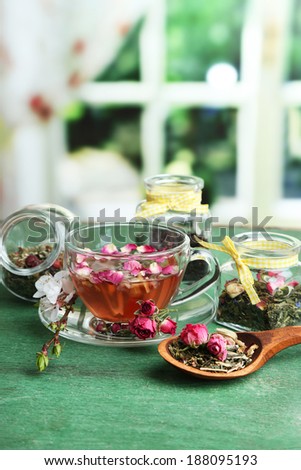 Assortment of herbs,  tea in glass jars and hot drink in cup on wooden table, on bright background