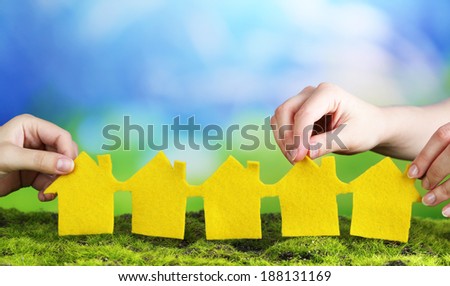 Hands hold houses on grass on natural background