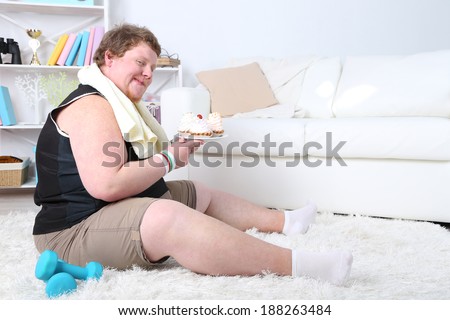 Large fitness man eating unhealthy food and trying to take exercise  at home