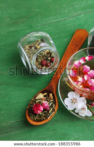 Assortment of herbs, tea in glass jars and cup of hot drink on wooden background