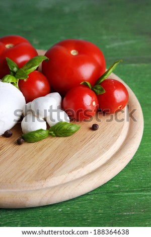 Composition with tasty mozzarella cheese balls, basil and red tomatoes, olive oil on cutting board, on color wooden background