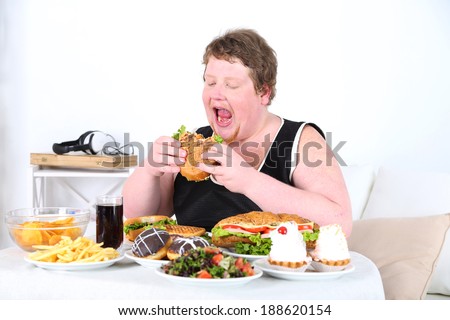 Fat man eating a lot of unhealthy food, on home interior background