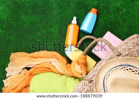 Wicker bag with colorful scarf, towel, bottles of lotions on  green background.