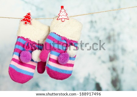Striped mittens hanging on clothesline on bright background
