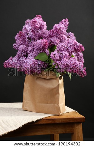 Beautiful lilac flowers in paper bag on wooden table on black background