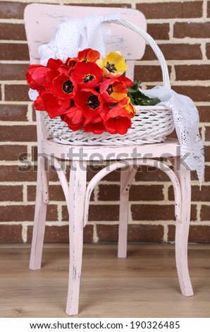 Bouquet of colorful tulips in wicker basket, on chair, on home interior background