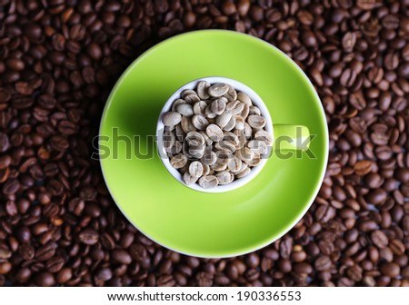 Cup full of green coffee beans on brown coffee beans background