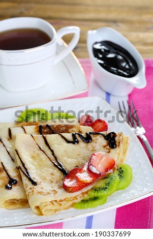 Delicious pancakes with strawberries and chocolate on plate on table