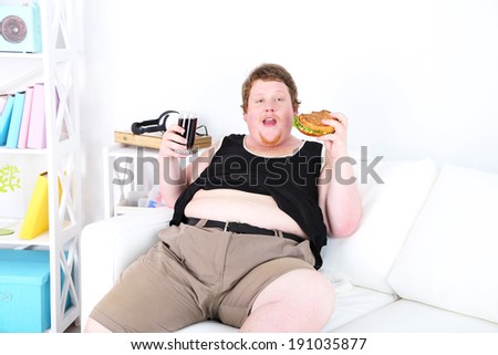 Fat man eating tasty sandwich and drink coke on home interior background
