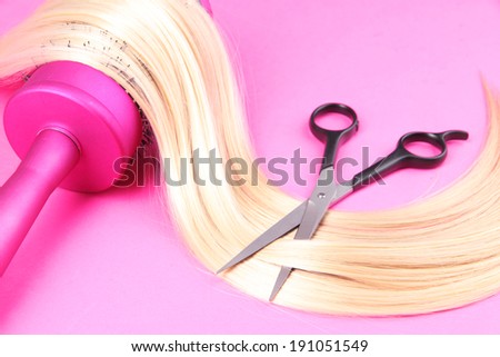 Long blond hair with hairbrush and scissors on pink background