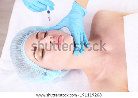 Woman in beauty clinic getting botox injection, on light background