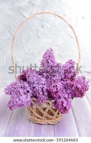 Beautiful lilac flowers in wicker basket on table on light background