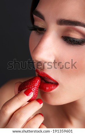 Girl with red lips, nails and strawberries on dark background