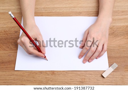 Human hands with pencil writing on paper and erase rubber on wooden table background