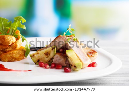 Grilled meat  with fried potato and marrow pieces and pomegranate seeds on plate, on wooden table on bright background