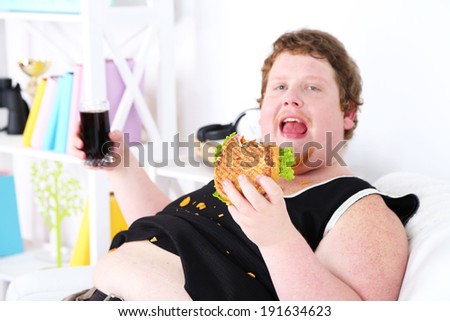 Fat man eating tasty sandwich and drink coke on home interior background
