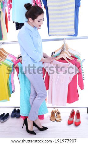 Young woman choose clothes near rack with hangers
