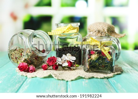 Assortment of herbs and tea in glass jars on wooden table, on bright background