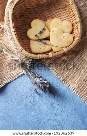 Lavender cookies in wicker basket, on sackcloth, on color wooden background